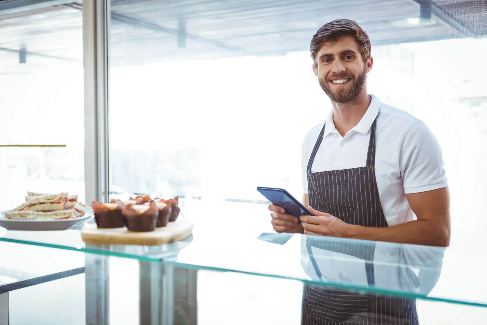 fröhlicher Mann vor einer Glastheke in einem Gastronomie-Unternehmen, arbeitet mit dem Kassensystem von GastroSoft