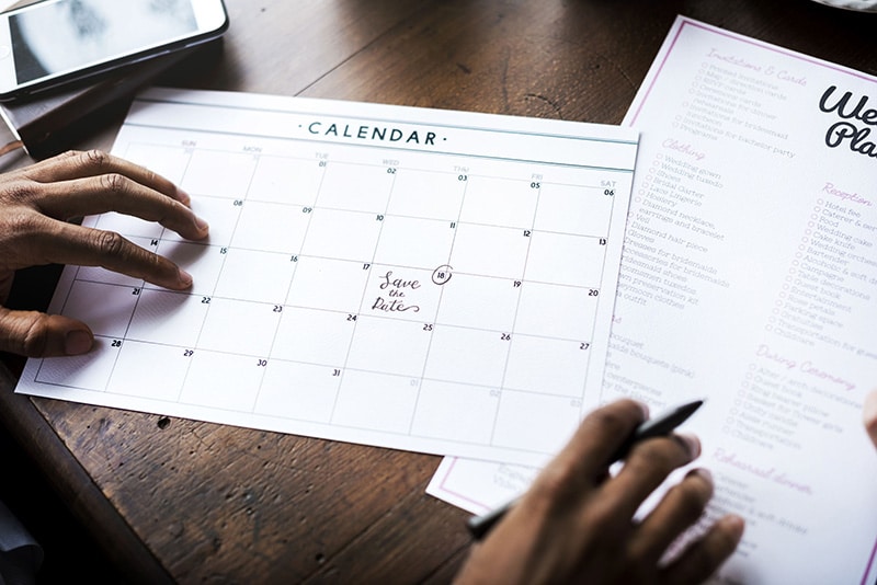 Kalender auf Papier mit Events die über die Event Erweiterung geplant wurden, im Hintergrund auf dem Tisch ein Smartphone