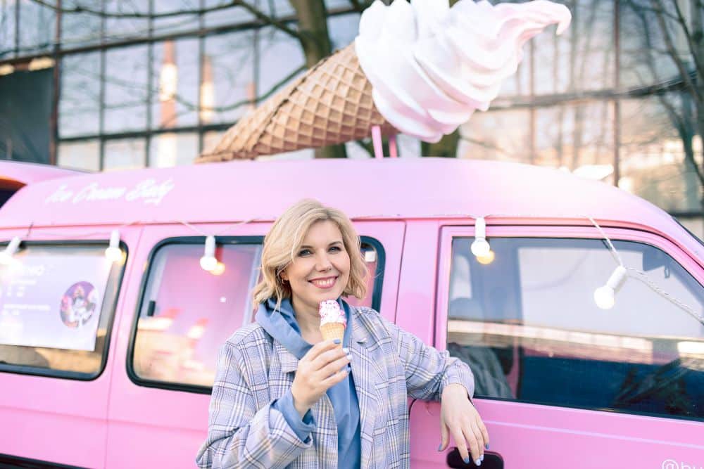Lächelnde Frau hält Eis und steht vor pinkem Eiswagen - mobile Eisdiele eröffnen