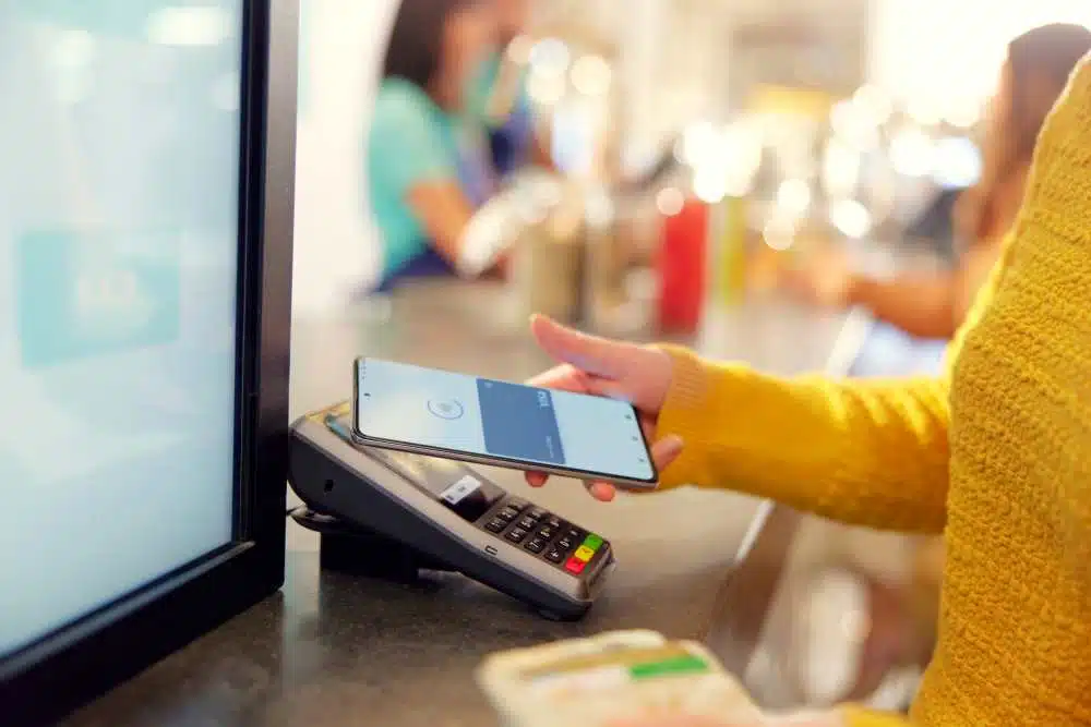 Frau hält ihr Smartphone an ein Kartenlesegerät und bezahlt via mobile payment