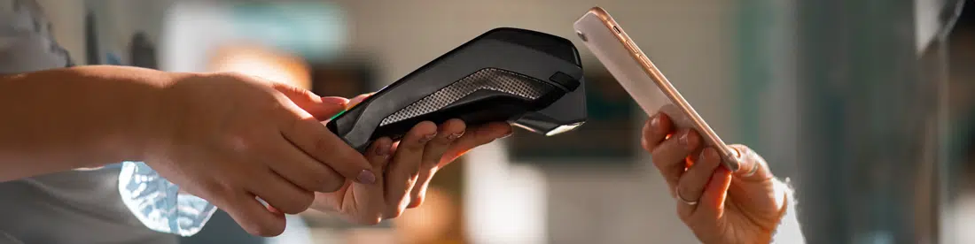 Junge Frau hält ihr Smartphone an ein mobiles Kartenterminal, das über das GastroSoft Kartenzahlung Add-On verfügt und zahlt kontaktlos