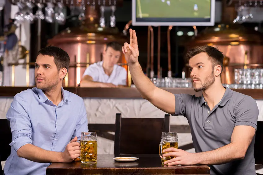 Zwei Männer mit Bier sitzend in einer Bar - einer ruft den Kellner, Schankmanagement Add-On Erweiterung der Kassensoftware